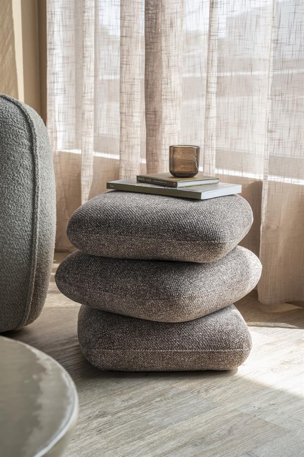 Sivohnedá taburetka By-Boo Pillowscape pri kresle v reálnom interiéri